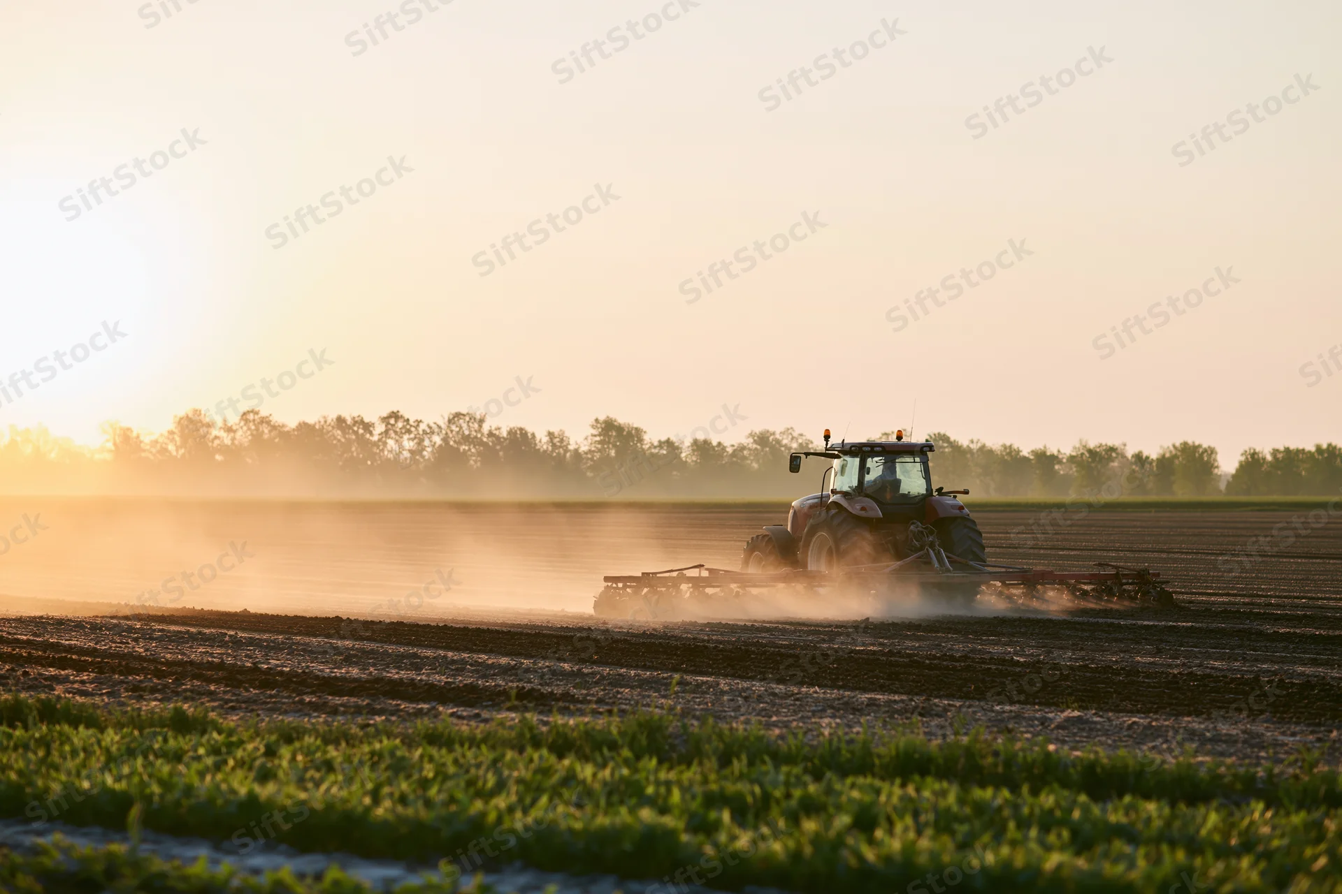 Tractor pulling disc harrow across flat farmland at sunset