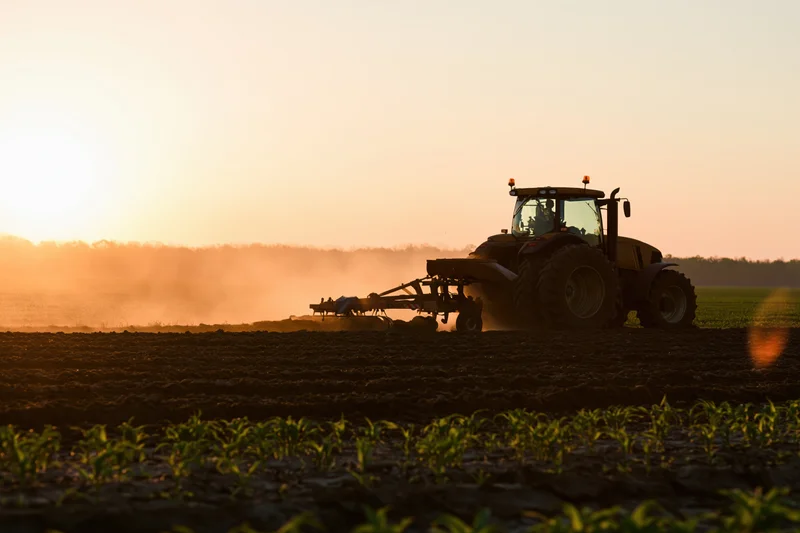Large farm tractor pulling a plow across a flat field