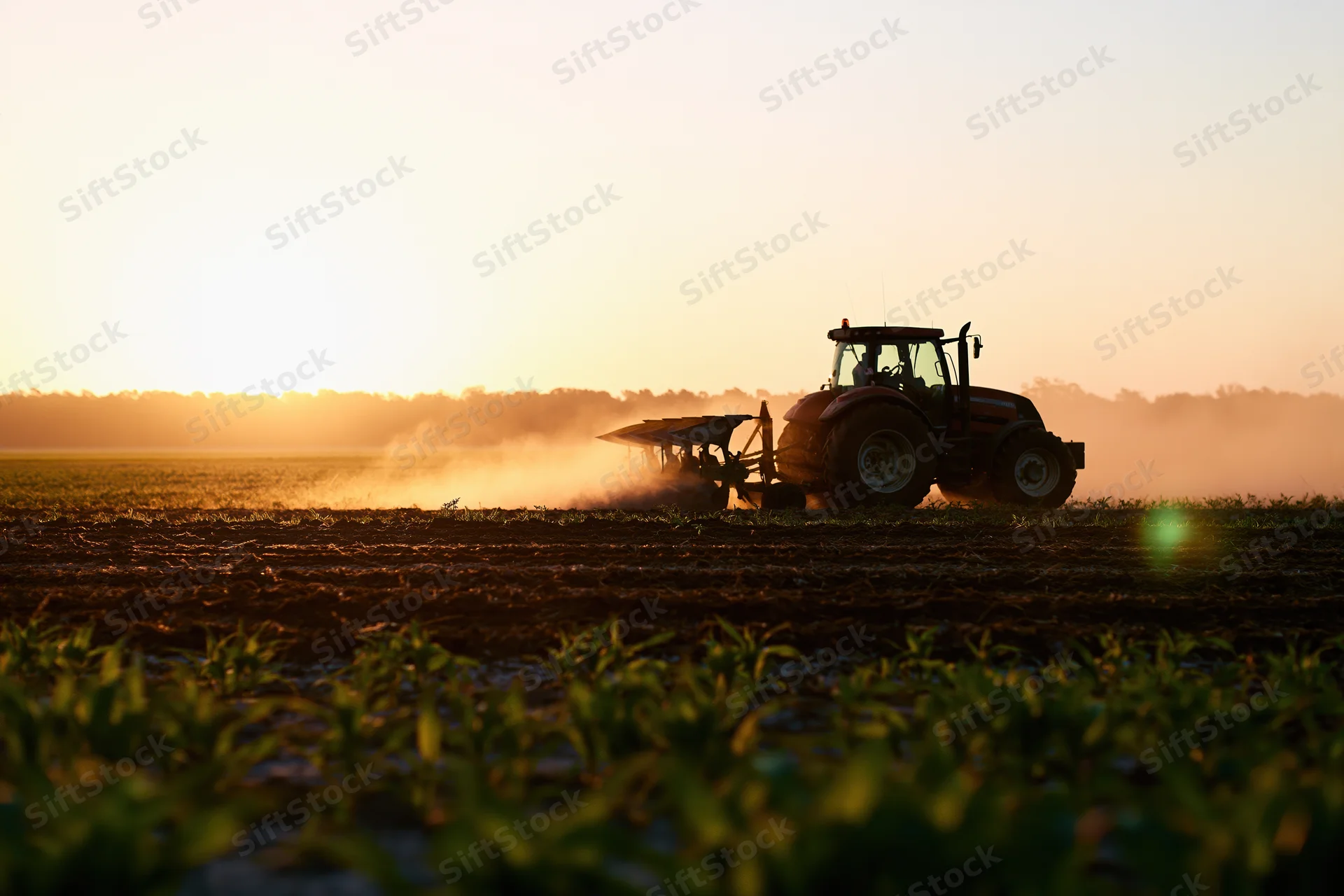 Tractor plowing a field at sunset in rural farmland
