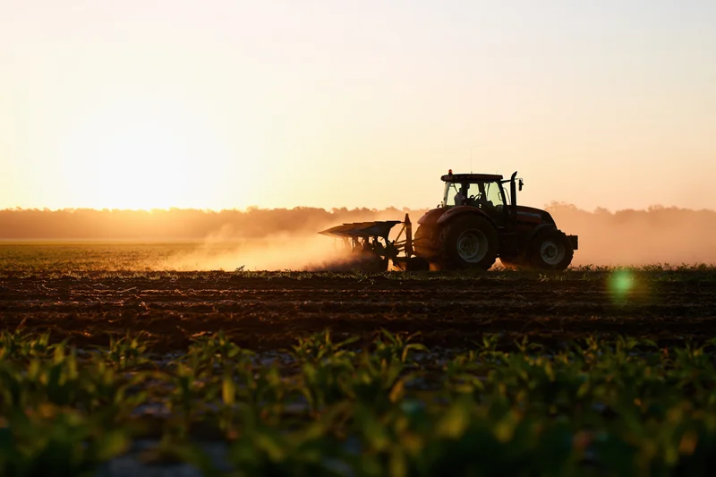 Tractor plowing a field at sunset in rural farmland
