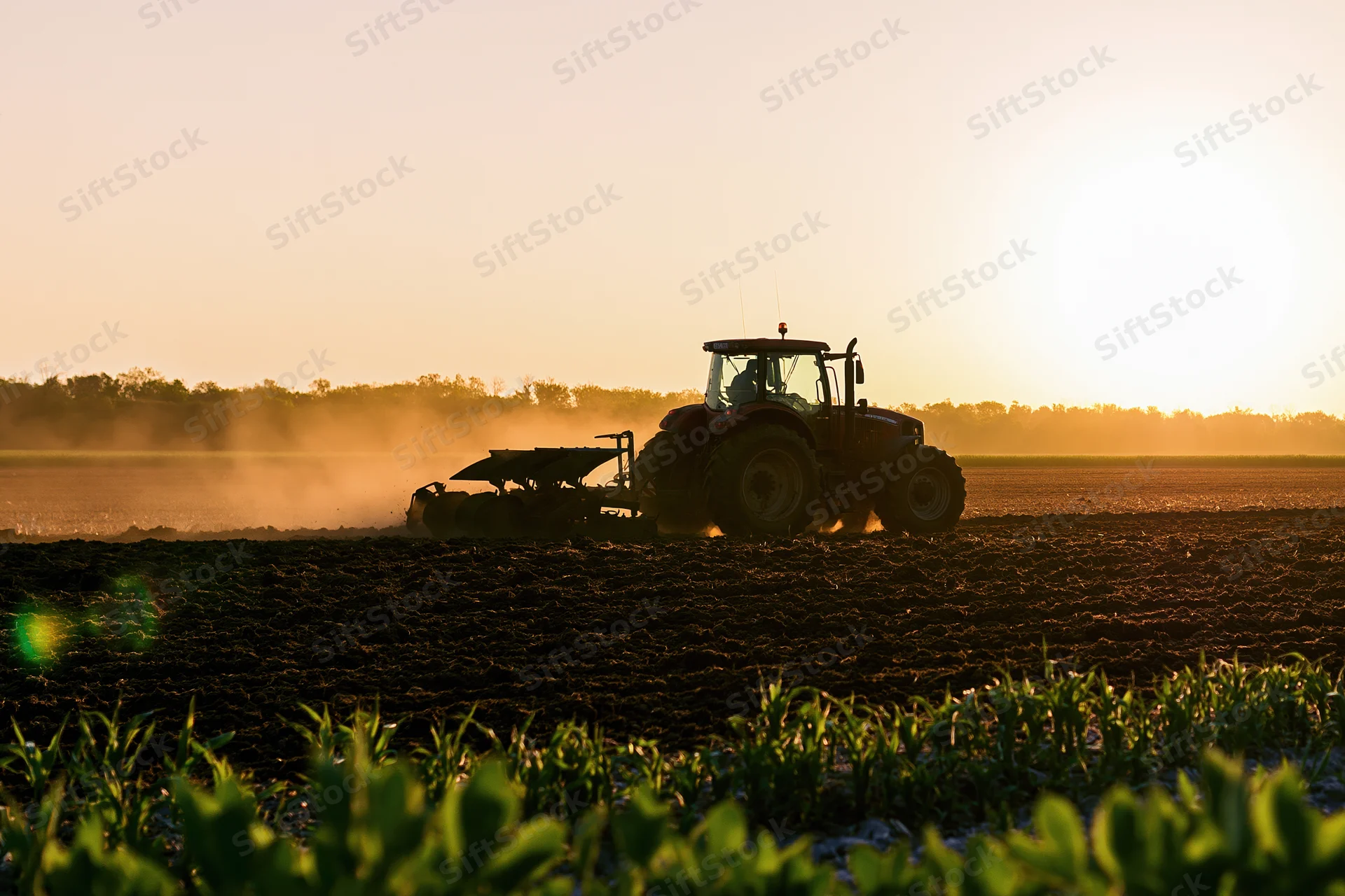 Tractor pulling a plow across a field at sunset