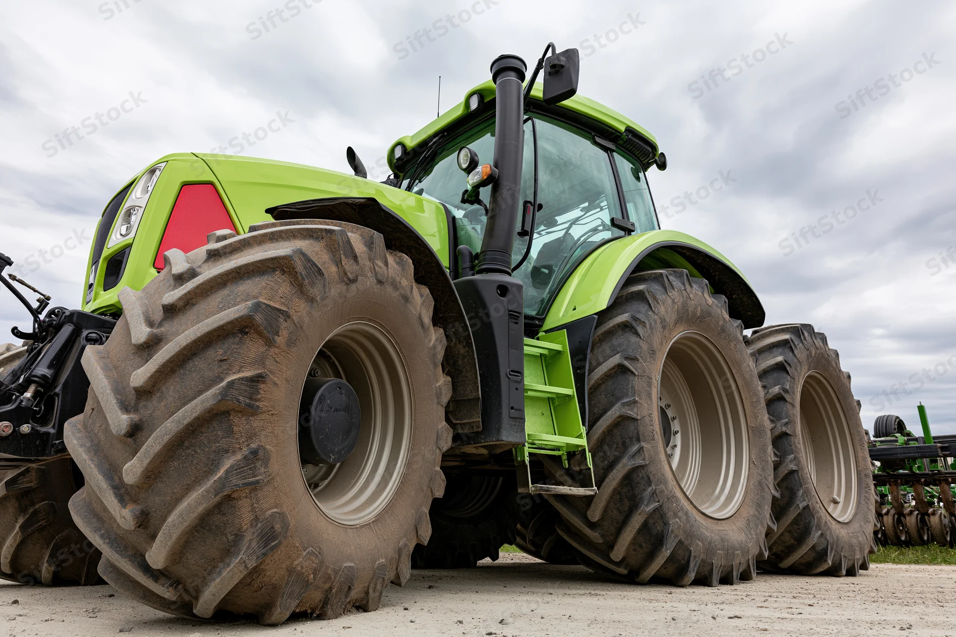Large modern green agricultural tractor parked outdoors on gravel with cloudy sky in background
