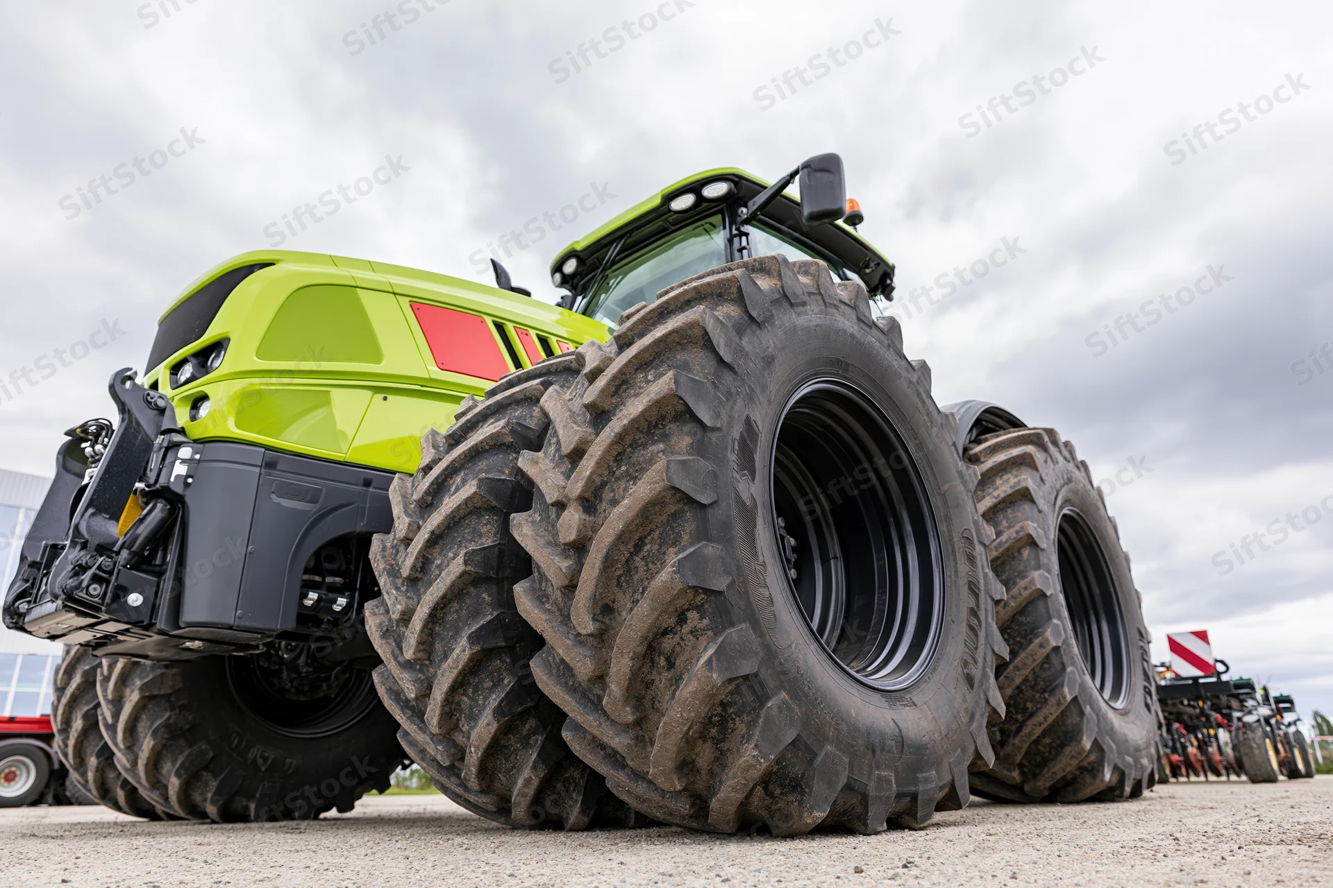 Large modern green agricultural tractor parked outdoors on gravel with large tires in a row of similar vehicles under cloudy sky
