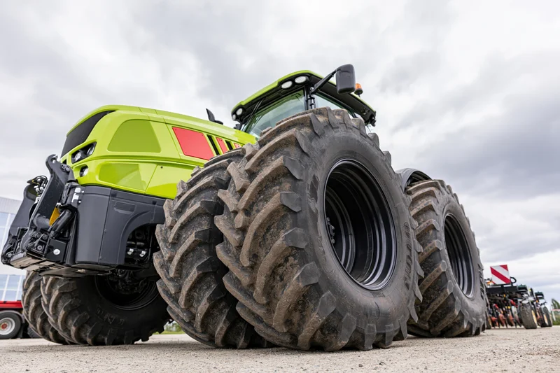 Large modern green agricultural tractor parked outdoors on gravel with large tires in a row of similar vehicles under cloudy sky
