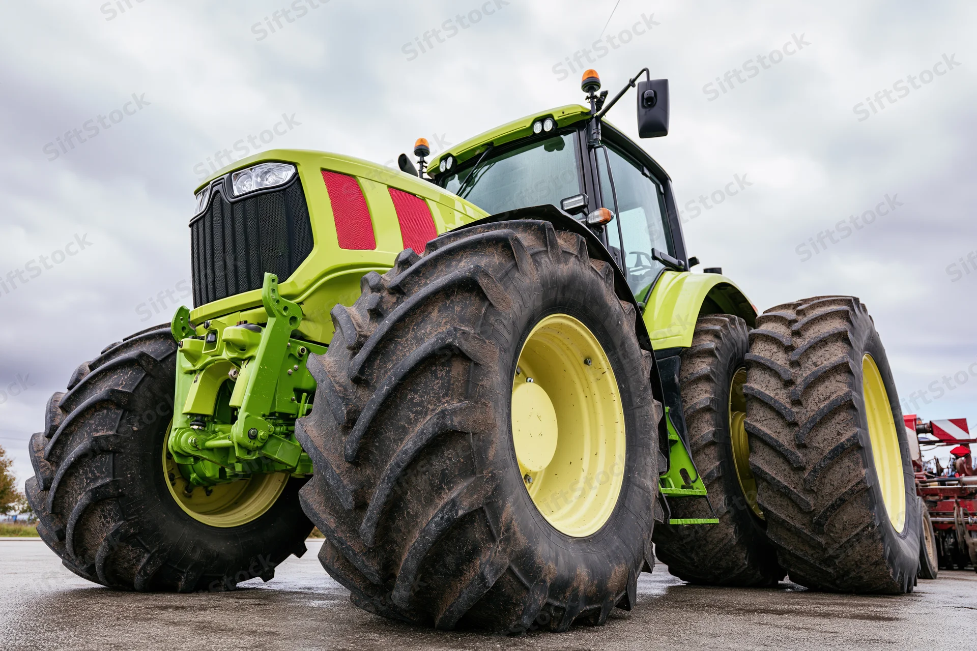 Large modern green agricultural tractor parked outdoors on asphalt under cloudy sky