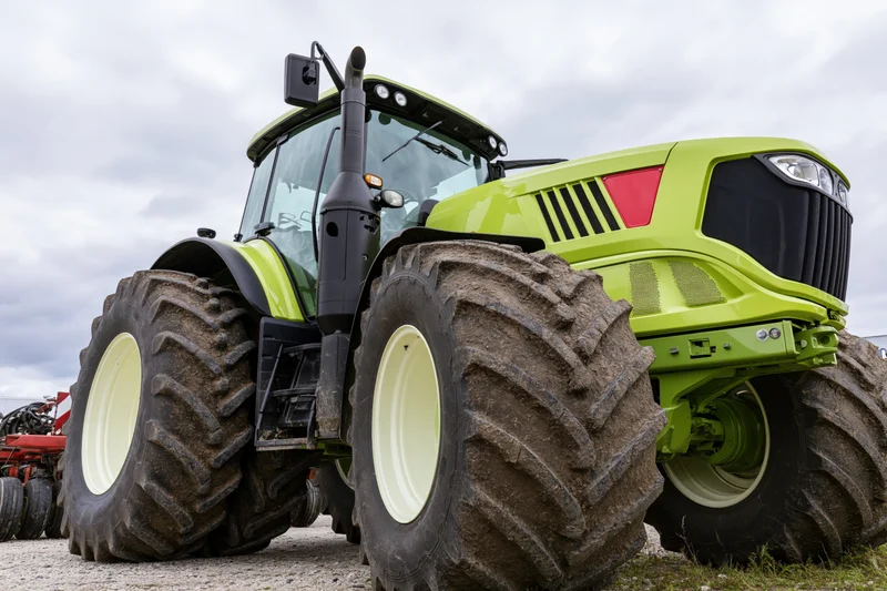 Large modern green agricultural tractor parked outdoors on gravel near field