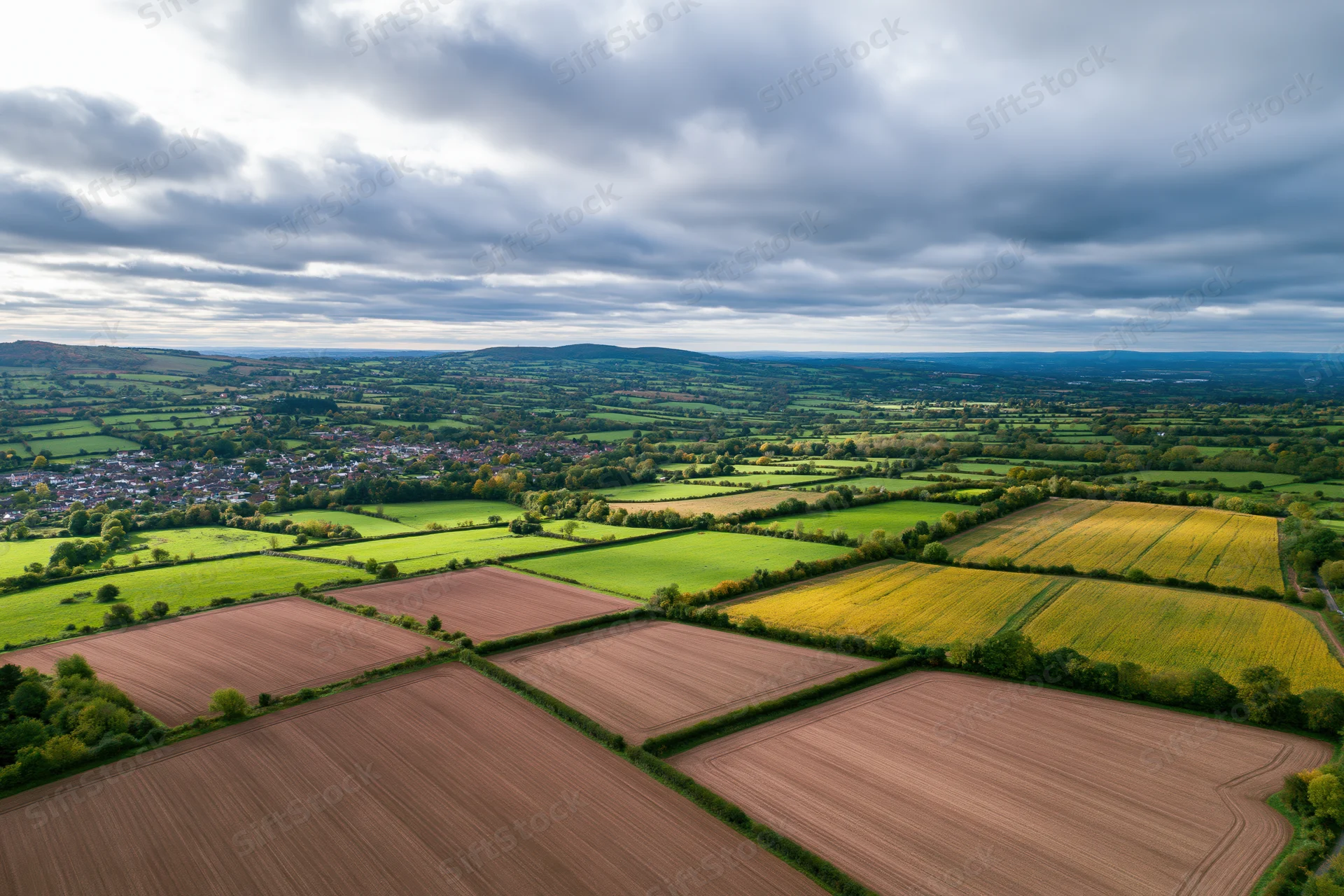 Aerial drone view of rolling english countryside with patchwork fields of crops and a village below