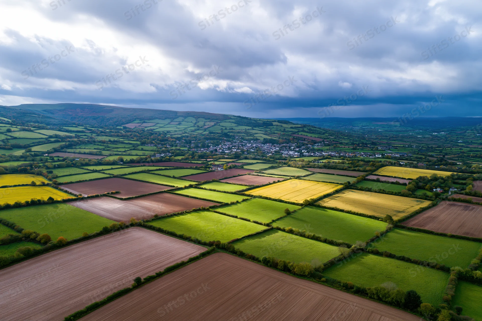Aerial drone view of patchwork farmland with green and yellow crops in rolling english countryside