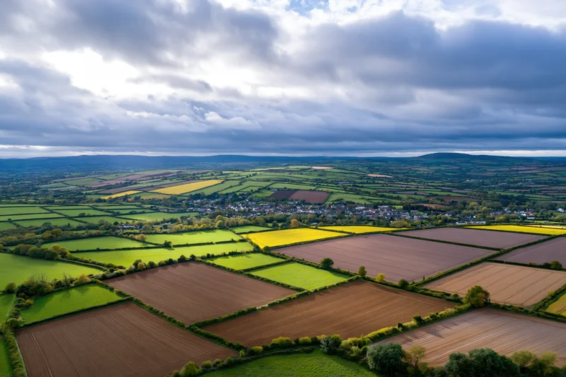 Aerial drone view of rolling english countryside with patchwork fields and a village below