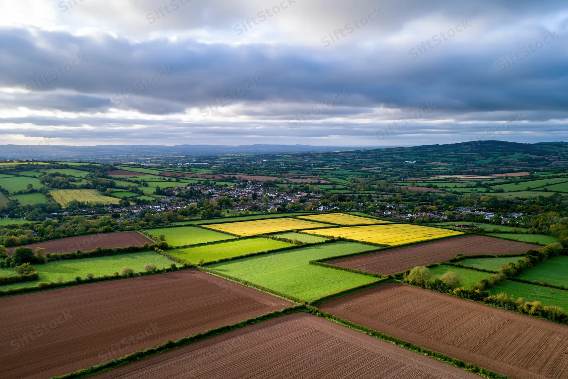 Aerial drone view of rolling english countryside with patchwork fields and a village below