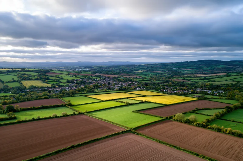 Aerial drone view of rolling english countryside with patchwork fields and a village below
