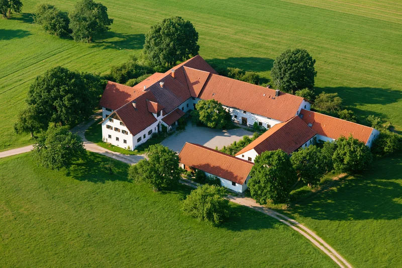 Aerial view of a white-walled bavarian farmstead with red tiled roofs surrounded by green fields and trees