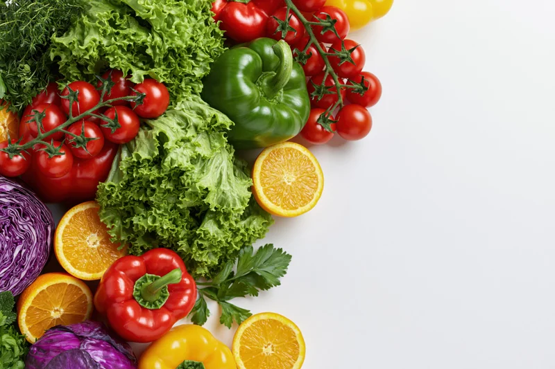 Fresh vegetables and fruits arranged loosely on white background with copyspace