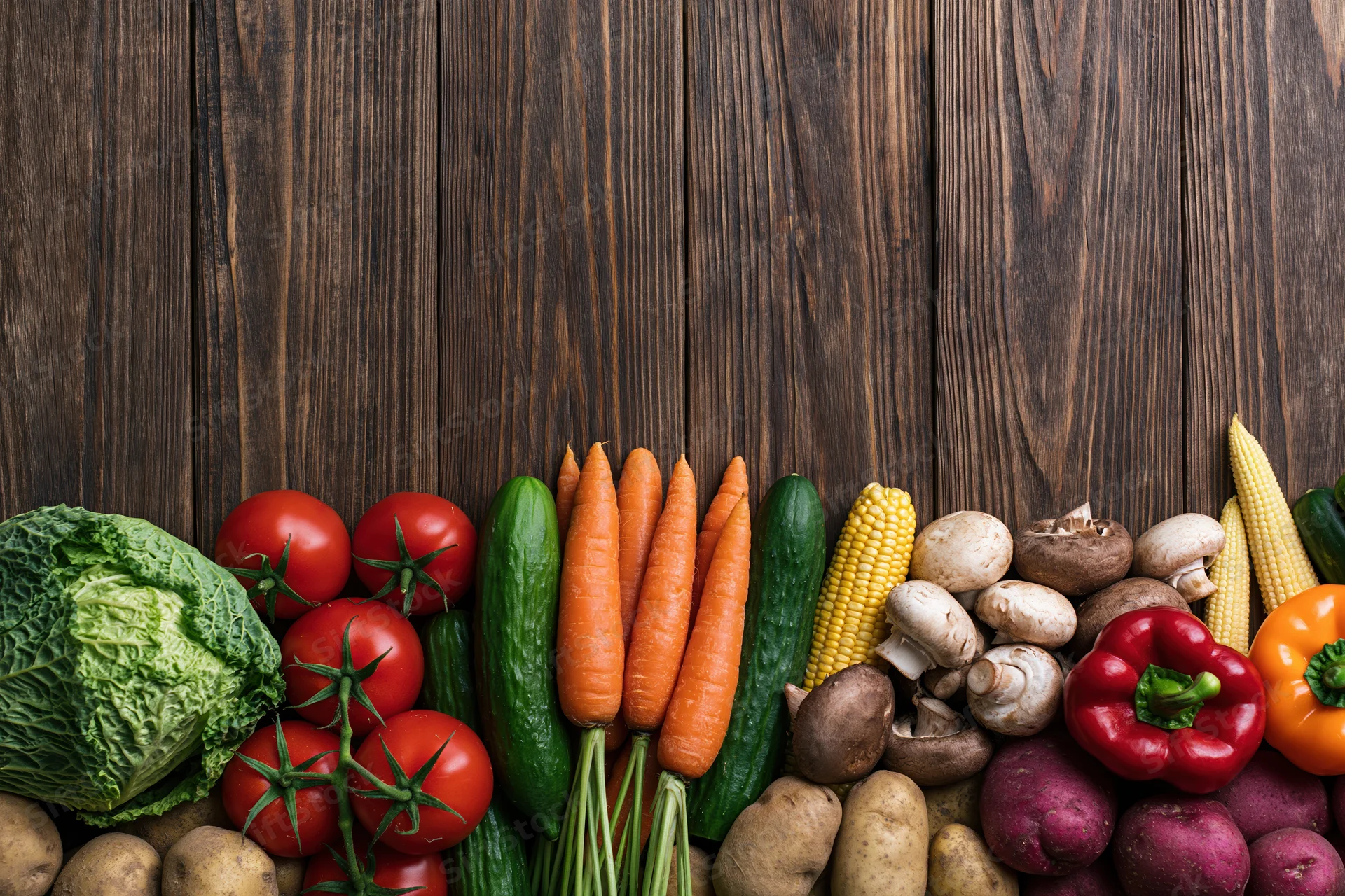 Assorted fresh vegetables arranged in a dense row along the bottom of a dark wooden surface with copyspace above