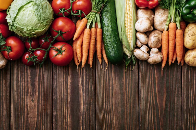 Fresh vegetables arranged in a dense row along the top of a dark wooden table with copyspace below