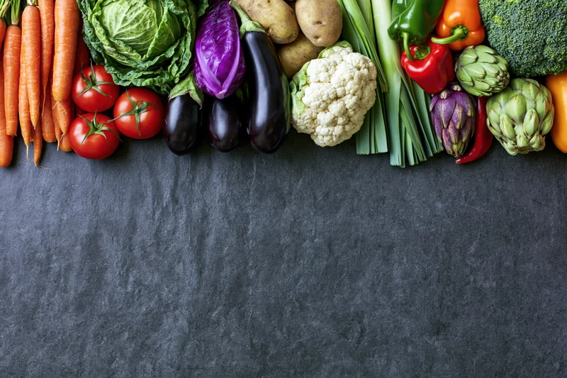 Assorted fresh vegetables arranged in a row on a dark surface with copyspace below
