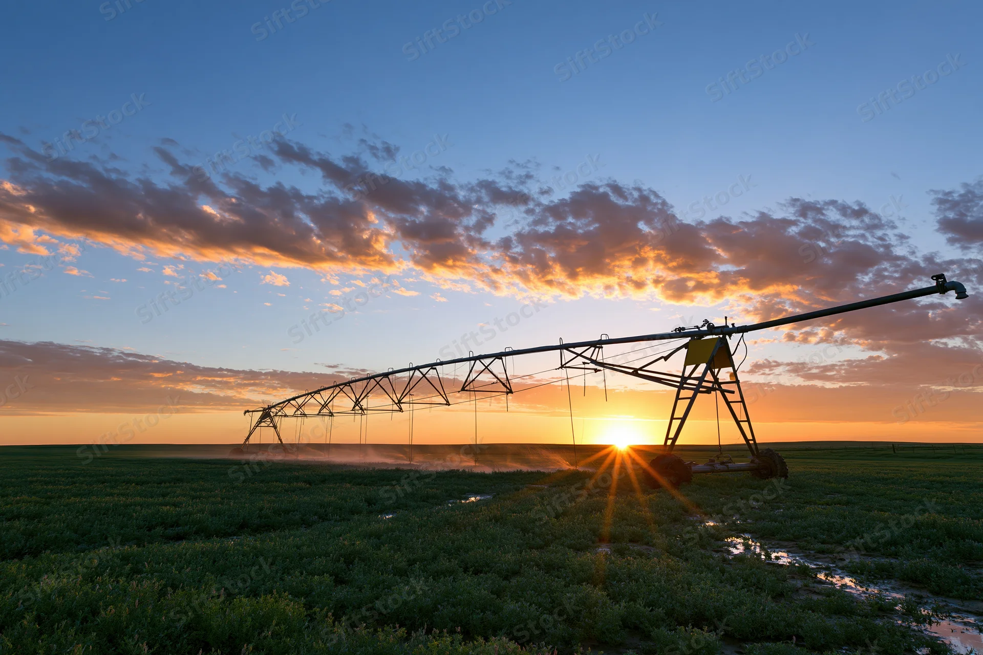 Center-pivot irrigation system watering a crop field at sunset