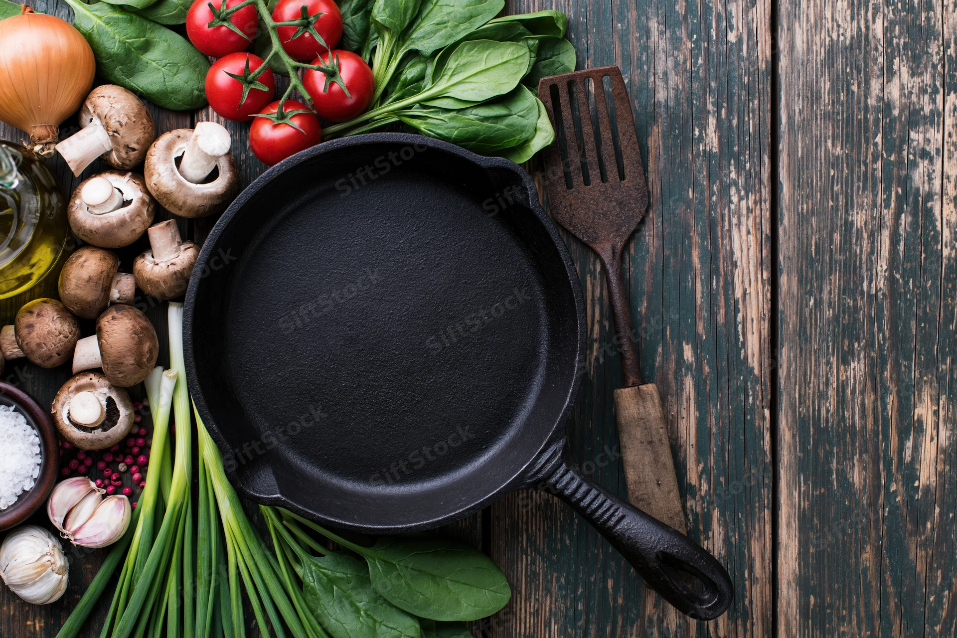 Empty cast iron skillet surrounded by fresh vegetables and cooking ingredients on a rustic wooden table