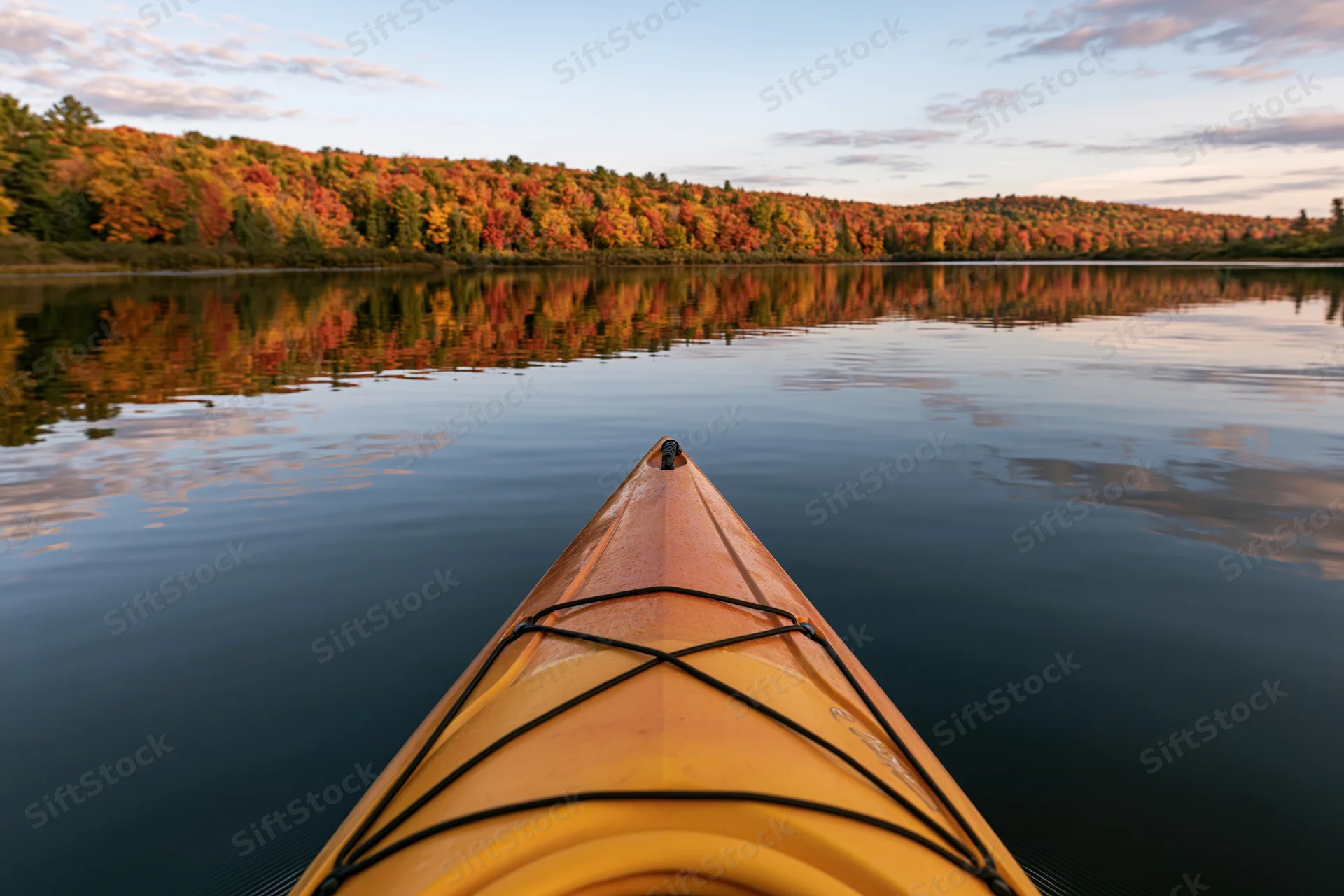 Yellow-orange kayak bow floating on calm lake with autumn forest reflection in water