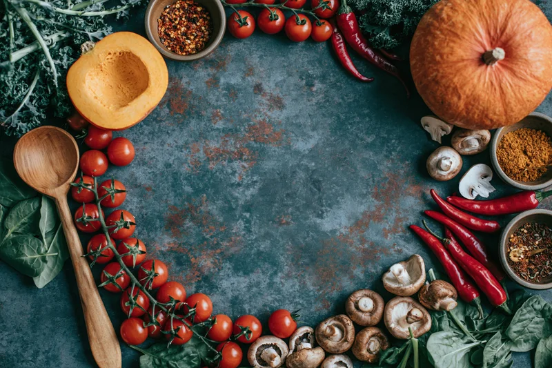 Autumn vegetables and cooking tools arranged in a flat lay frame on a dark textured surface with copyspace