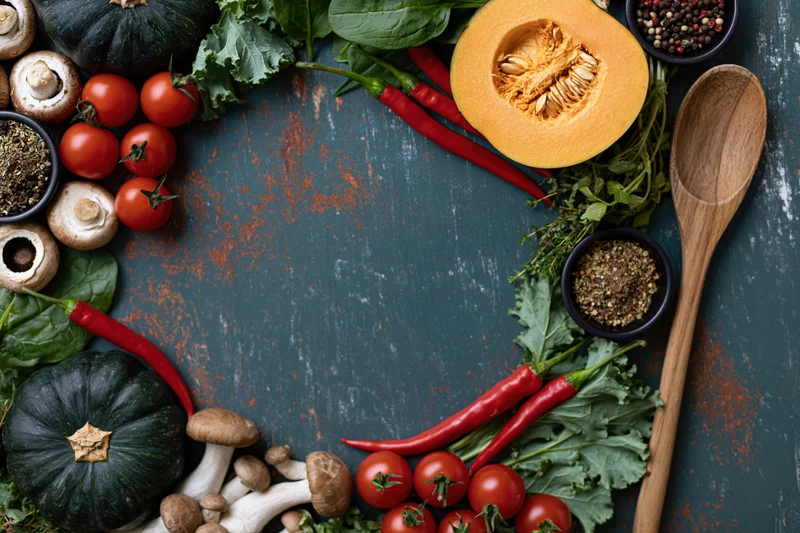 Autumn vegetables and cooking tools arranged in a flat lay on dark surface with copyspace