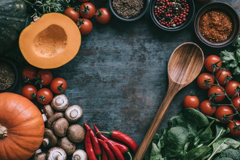 Autumn vegetables and cooking tools arranged in a flat lay on a dark textured surface with copyspace