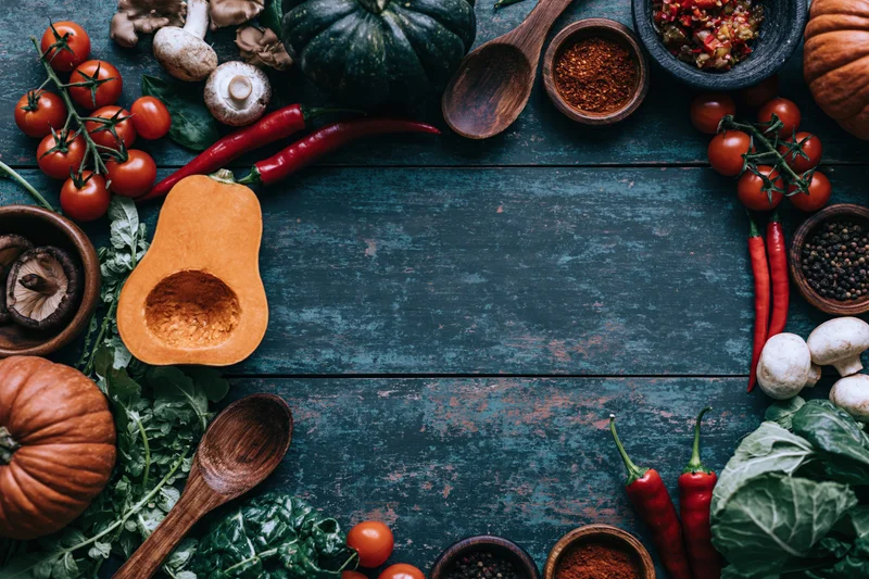 Autumn vegetables and cooking tools arranged in a frame on a dark wooden surface with copyspace in the center