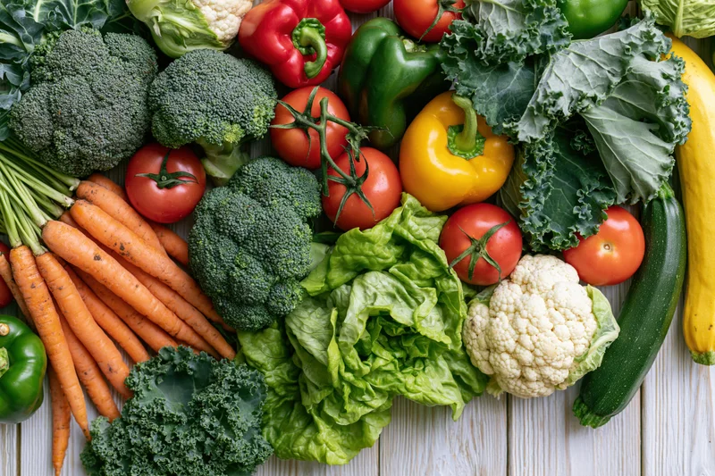 Fresh whole vegetables densely arranged on a light wooden surface in flat lay style