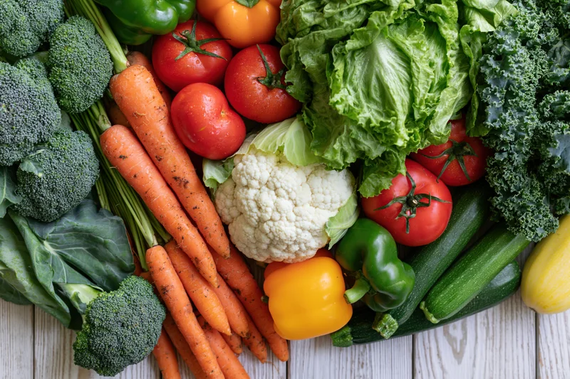 Fresh whole vegetables densely arranged on a light wooden surface in flat lay view