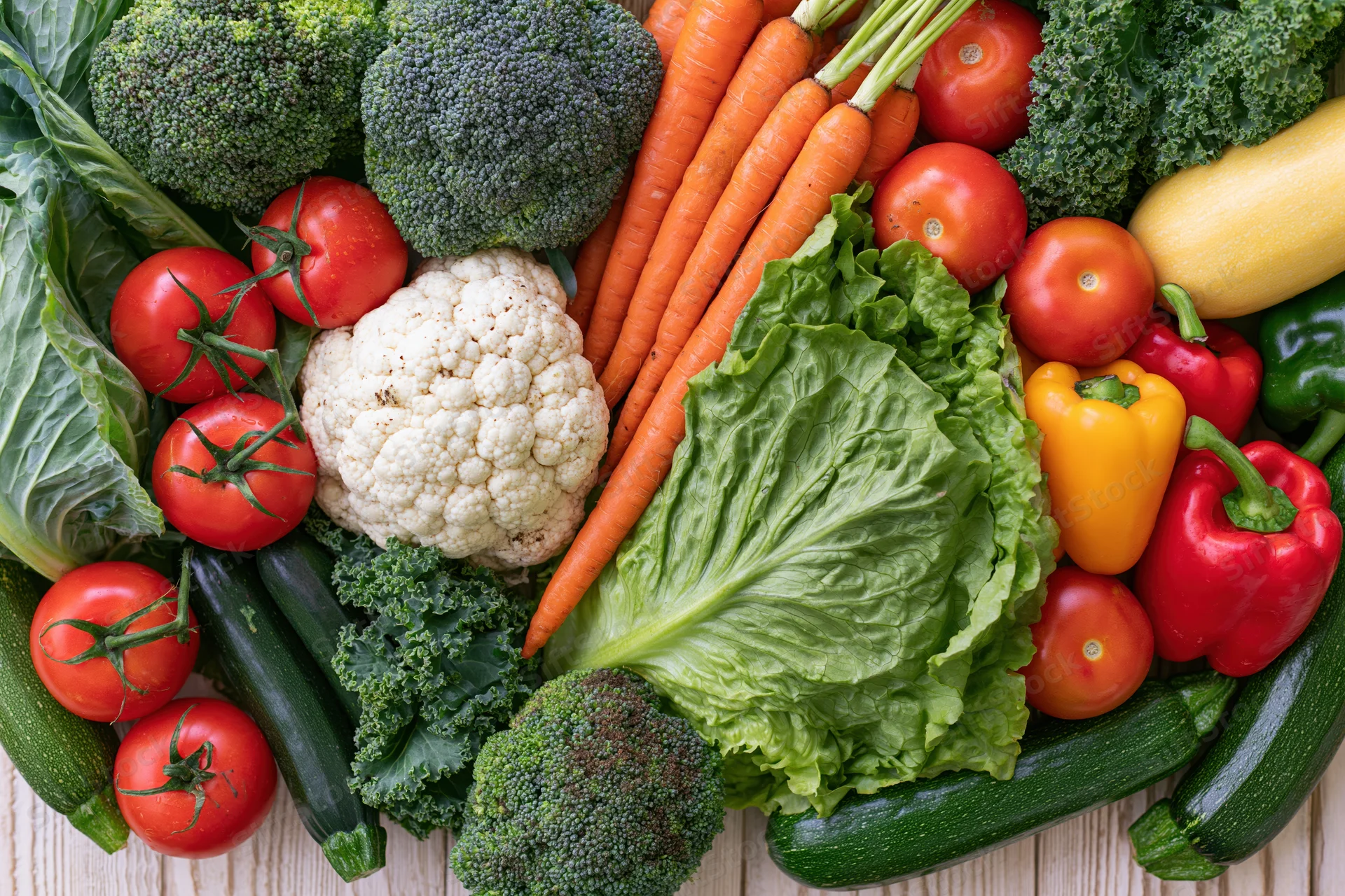 Fresh whole vegetables densely arranged on a light wooden surface