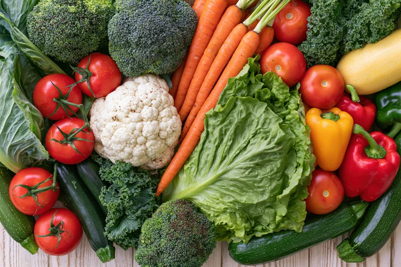 Fresh whole vegetables densely arranged on a light wooden surface