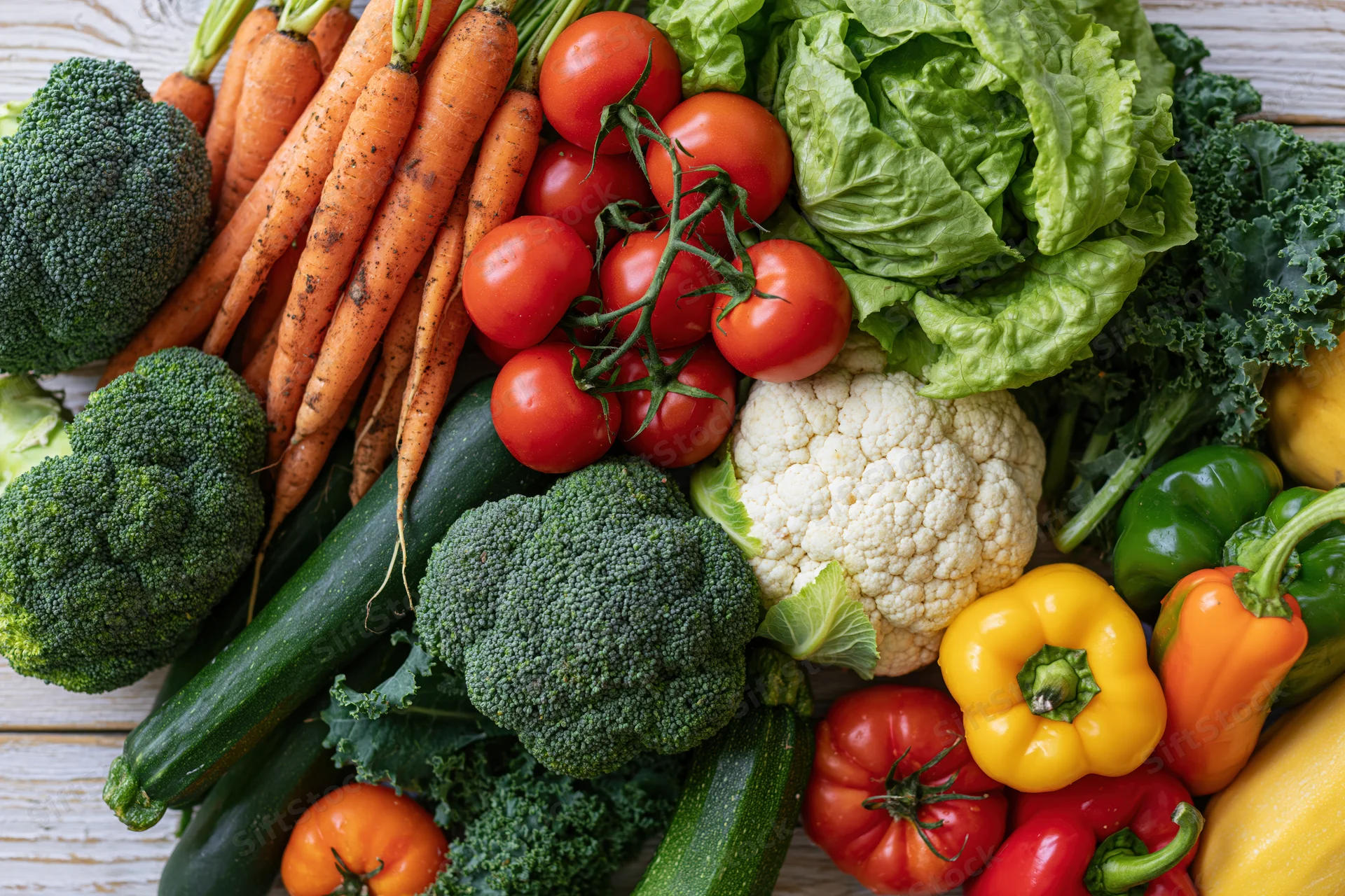 Fresh whole vegetables densely arranged on a light wooden surface