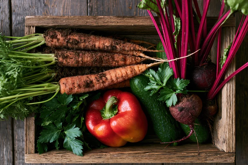 Fresh harvested vegetables arranged in a rustic wooden crate on a dark wood surface