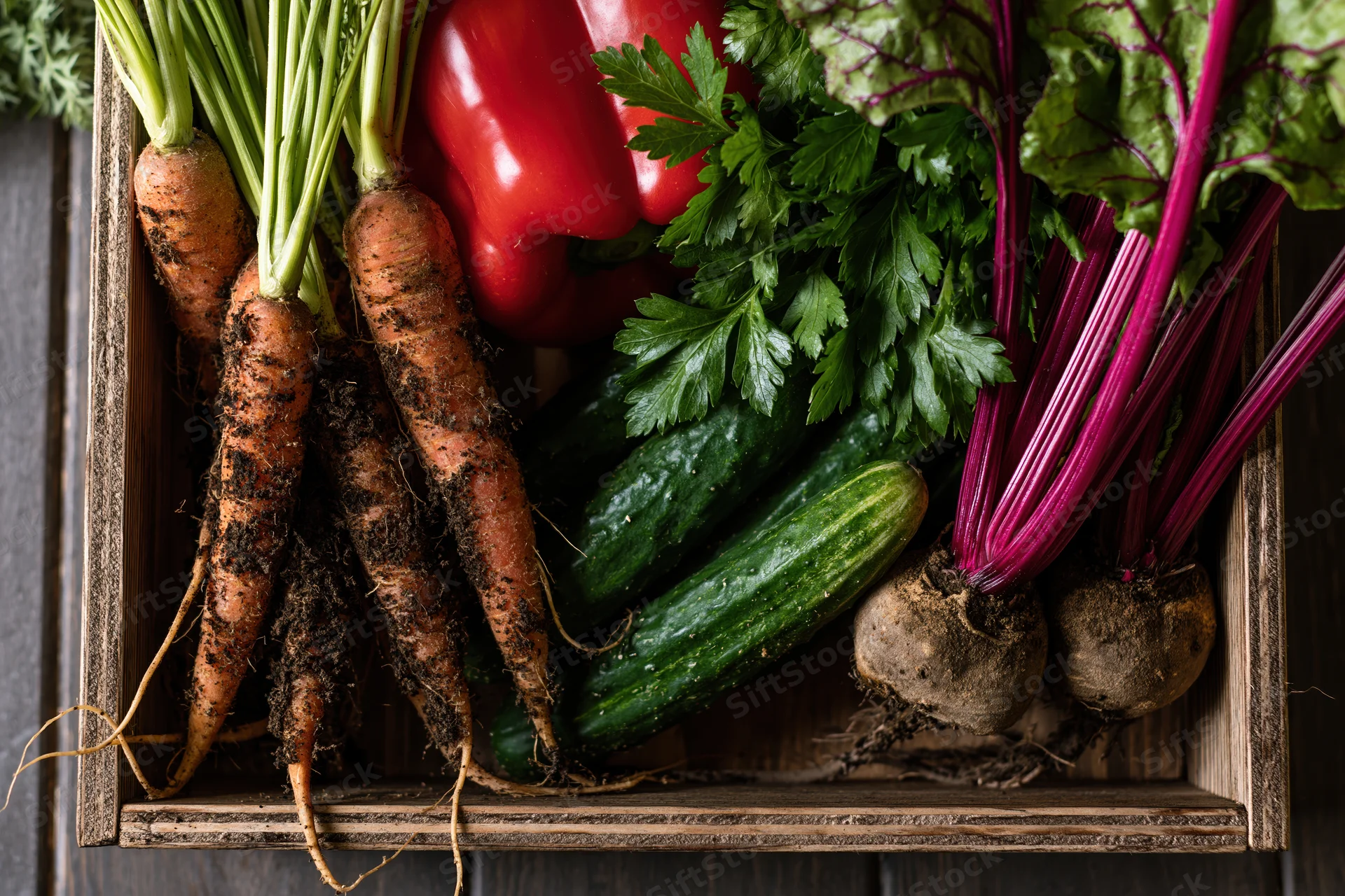 Fresh harvest vegetables arranged in a rustic wooden crate on dark wood surface