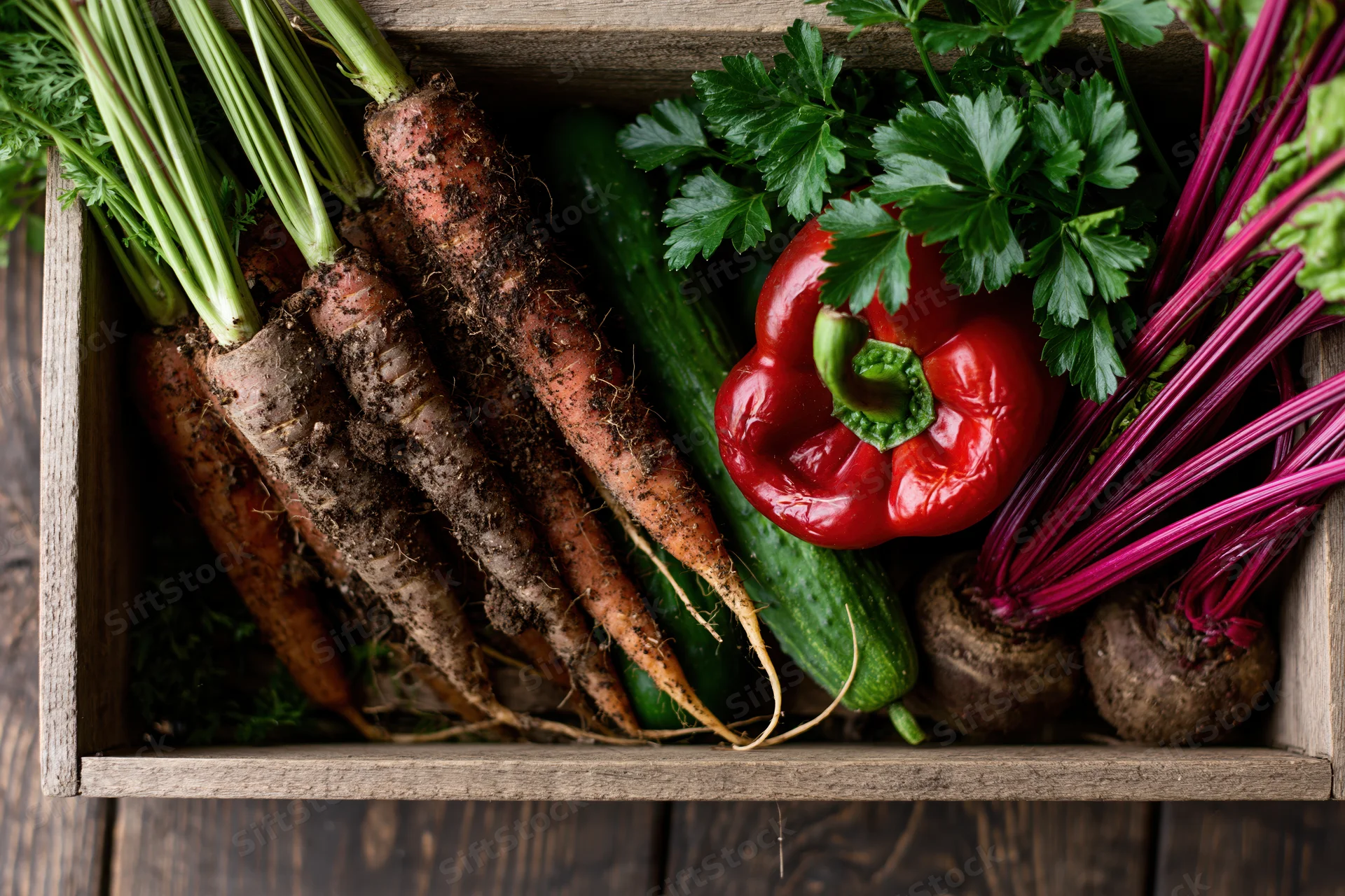 Fresh harvested vegetables arranged in a rustic wooden crate on a dark wood surface