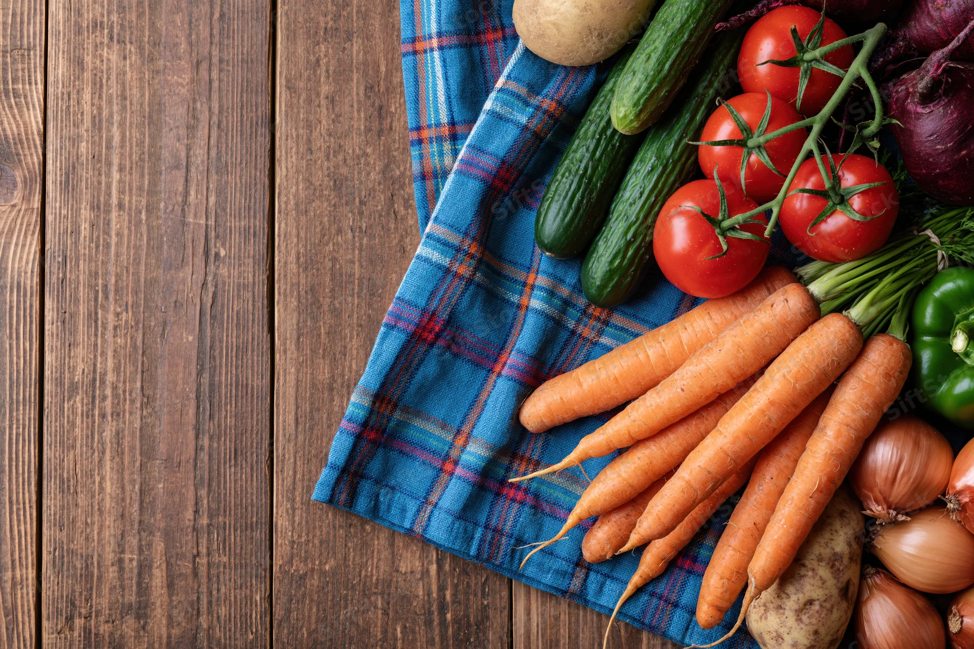 Fresh vegetables arranged on a blue plaid cloth on a rustic wooden table