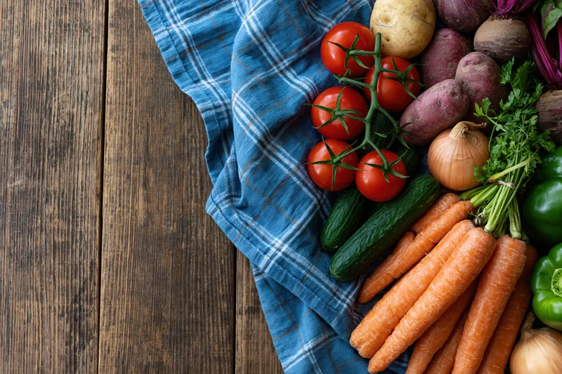 Fresh vegetables arranged on a blue plaid cloth on a rustic wooden table