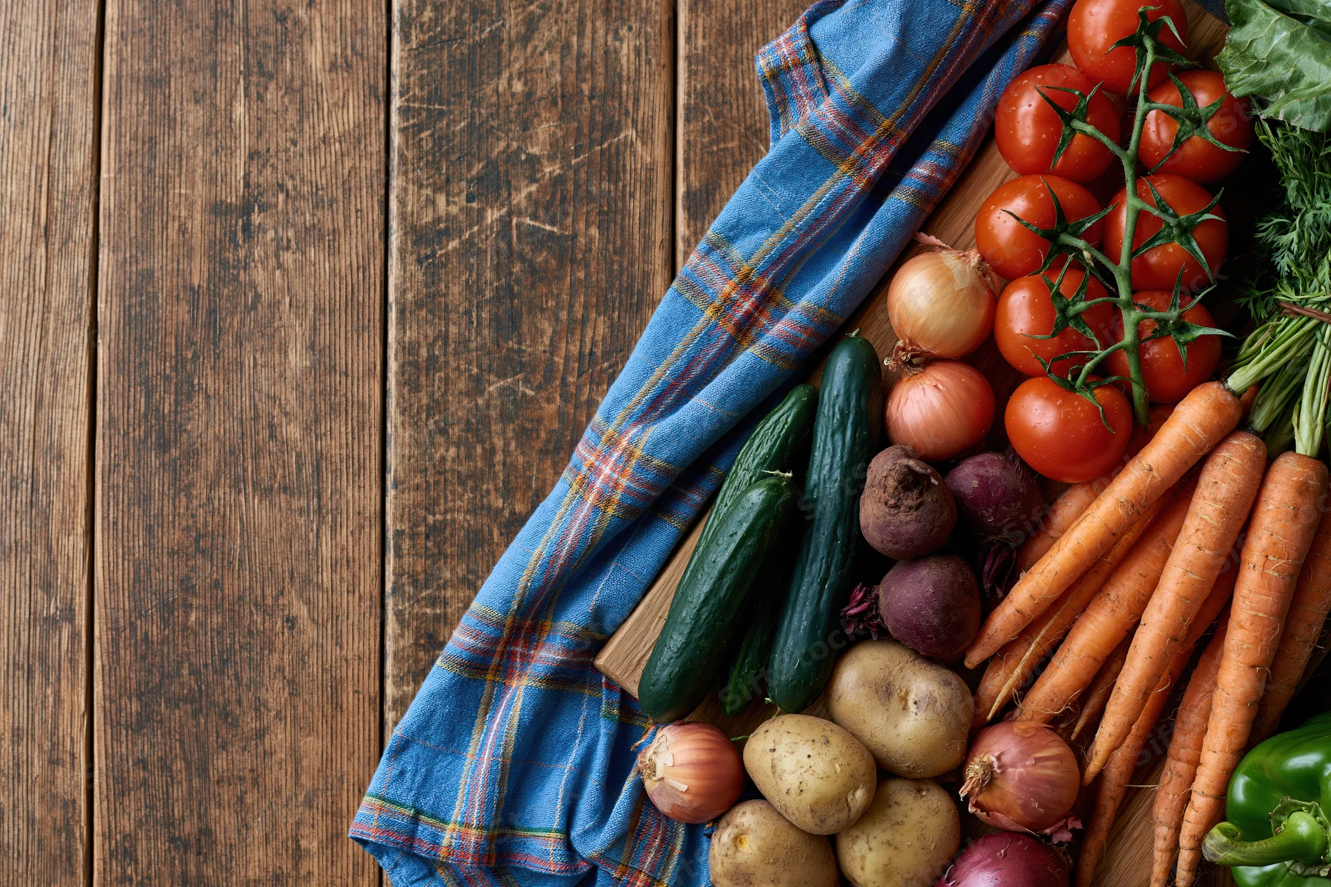 Fresh vegetables arranged on a wooden cutting board with a plaid cloth, on a rustic table