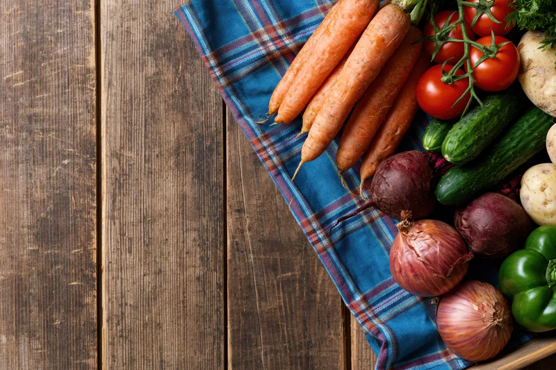 Fresh vegetables arranged on a blue plaid cloth on a rustic wooden table
