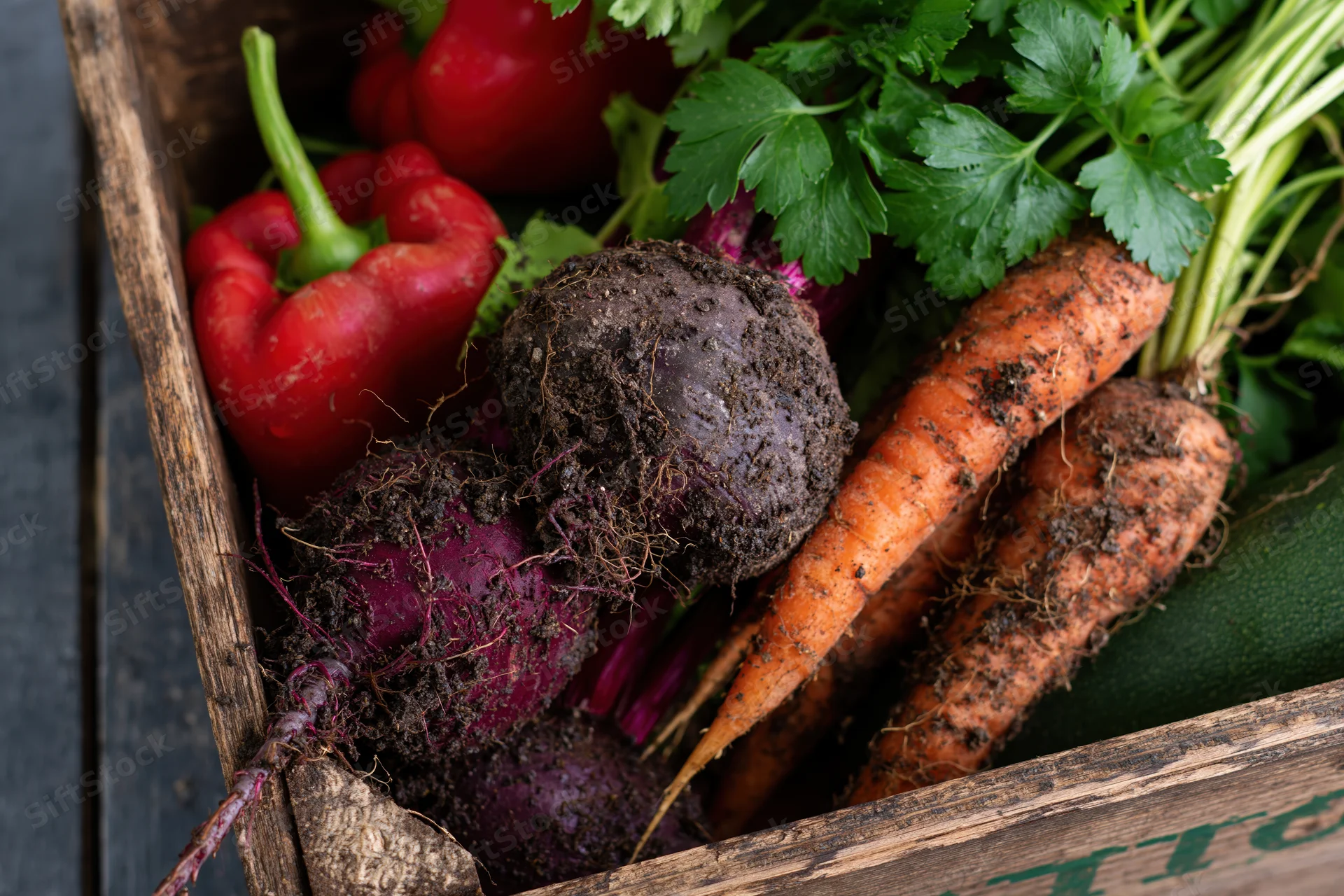 Freshly harvested vegetables with soil and roots in a wooden crate