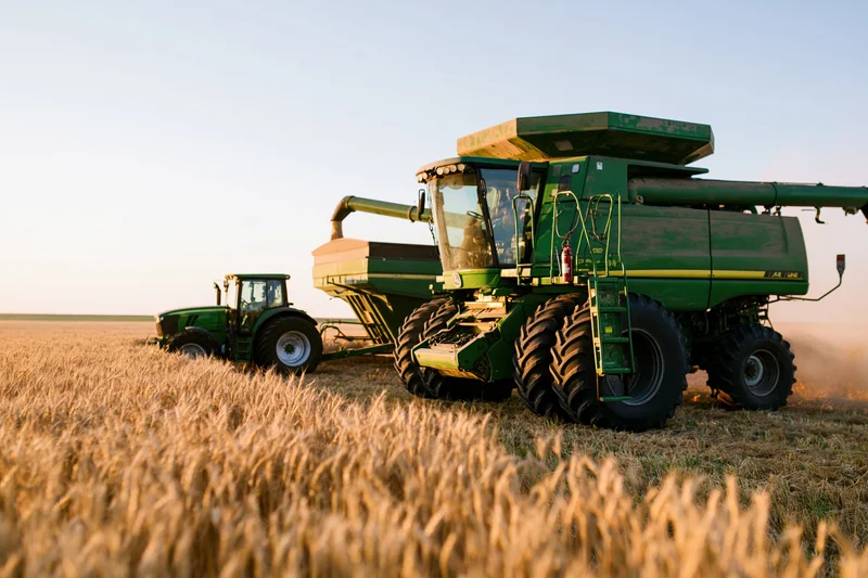 Green combine harvester transferring grain through auger into tractor trailer in wheat field at dusk