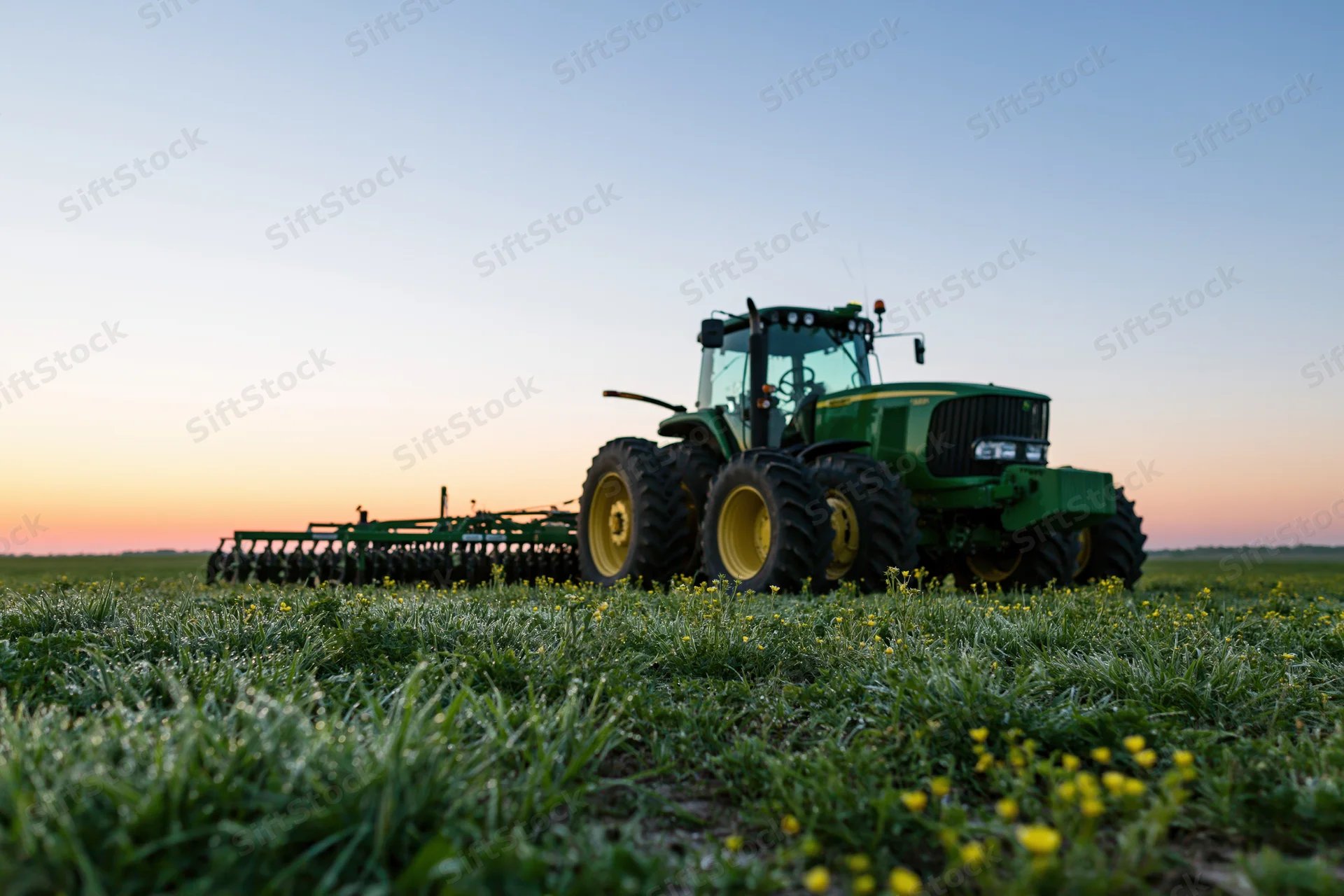 Green tractor with wide multirow planting attachment in a grassy field at sunset