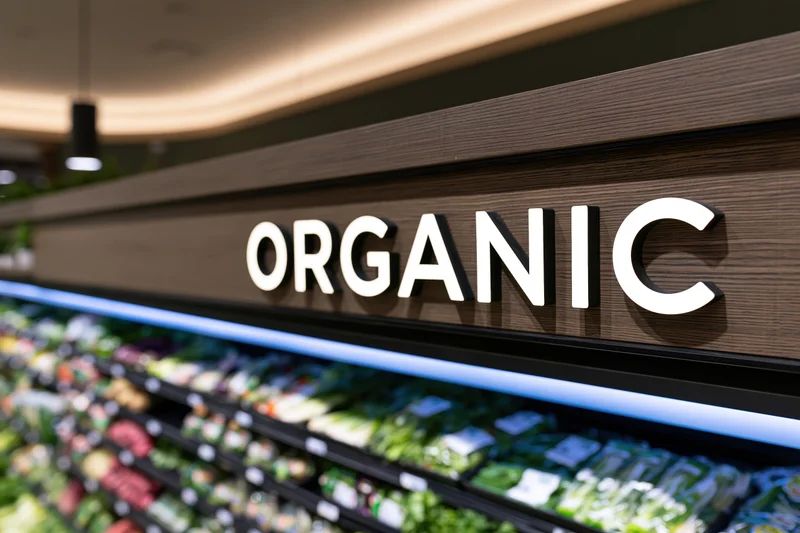 Illuminated organic sign above refrigerated produce display in grocery store