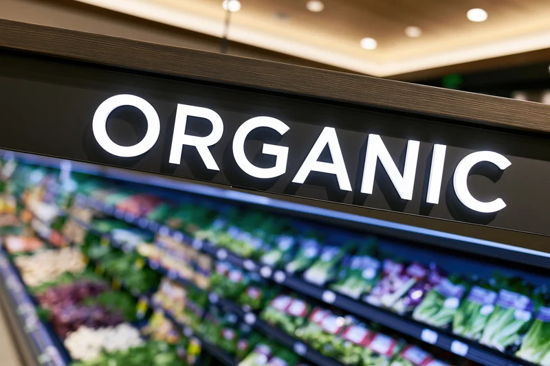 Illuminated organic sign above refrigerated produce display in grocery store