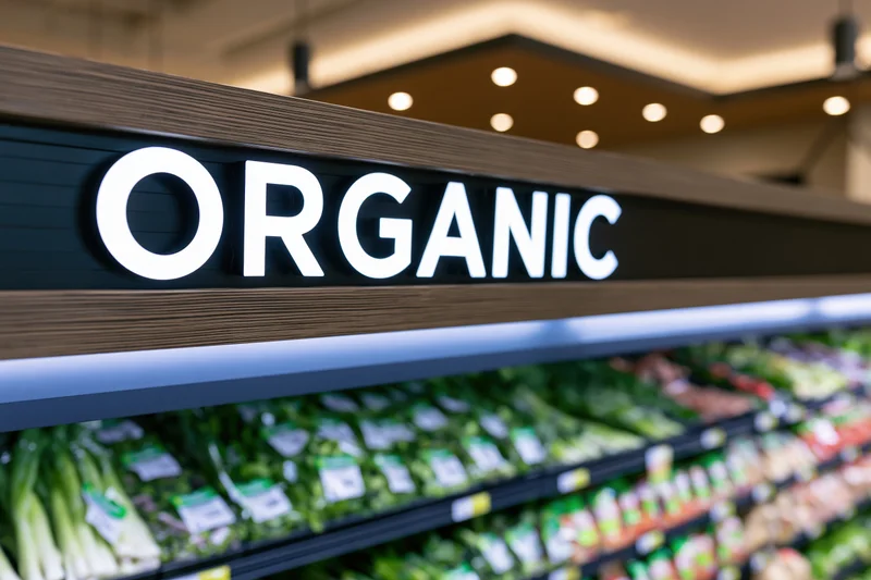 Illuminated organic sign above refrigerated produce shelves in a grocery store