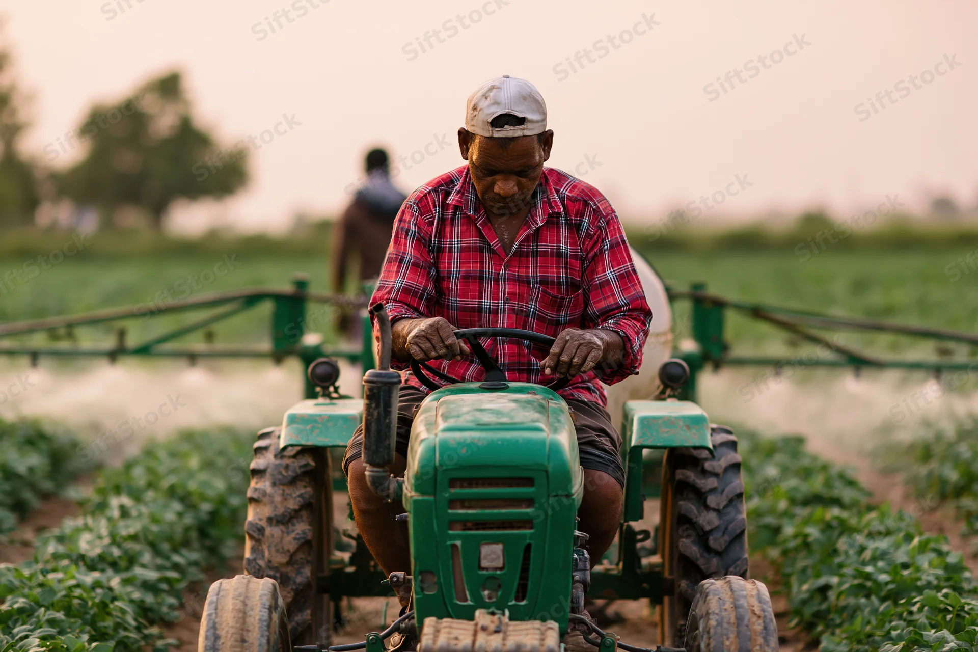 Indian farmer operating small green tractor with spray boom in crop field