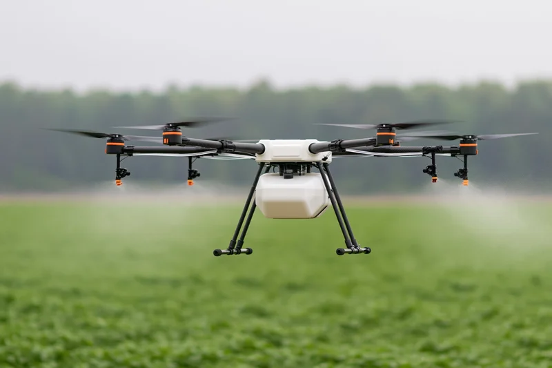 Agricultural sprayer drone hovering low over green crop field