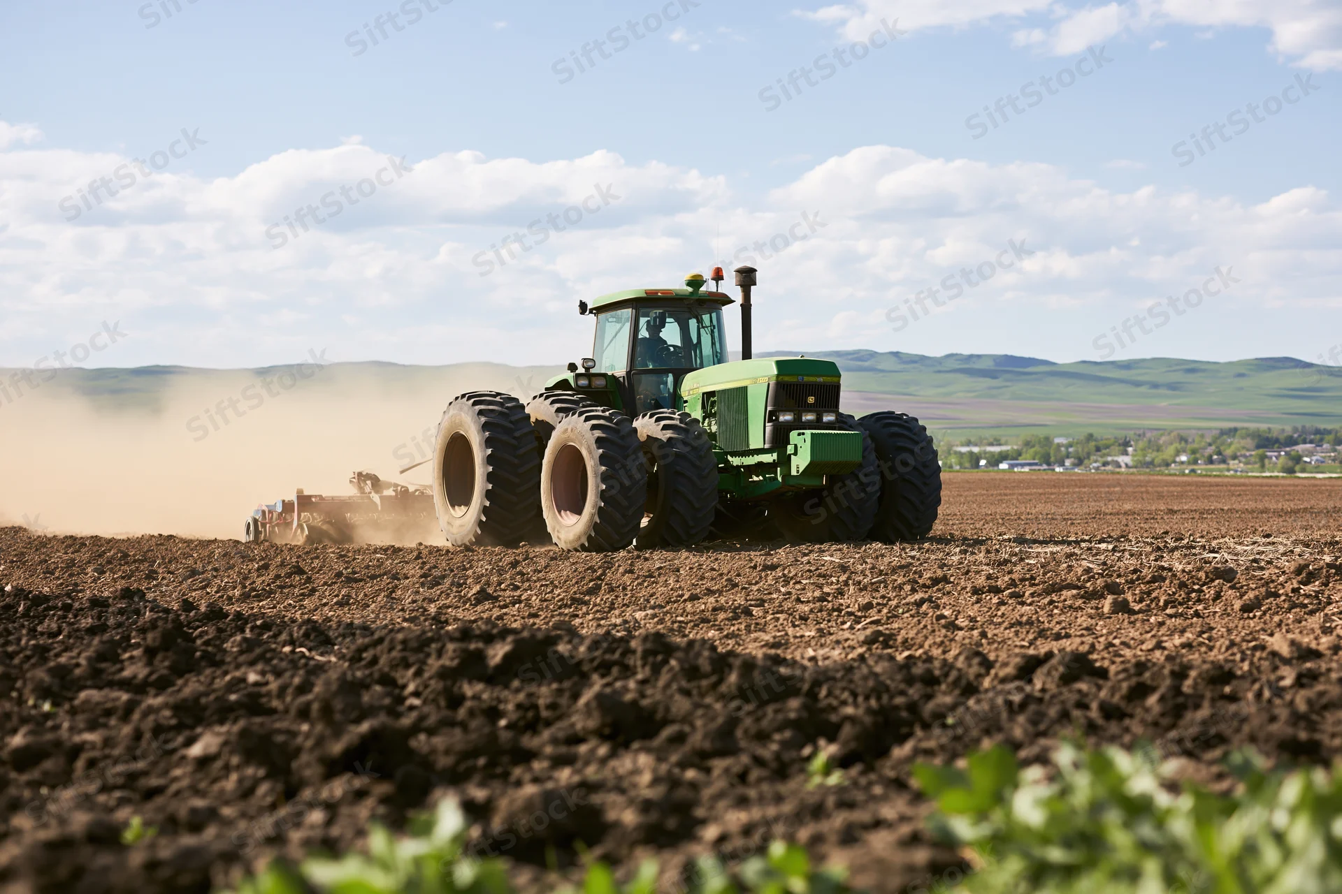Green tractor pulling seeder across tilled field under partly cloudy sky