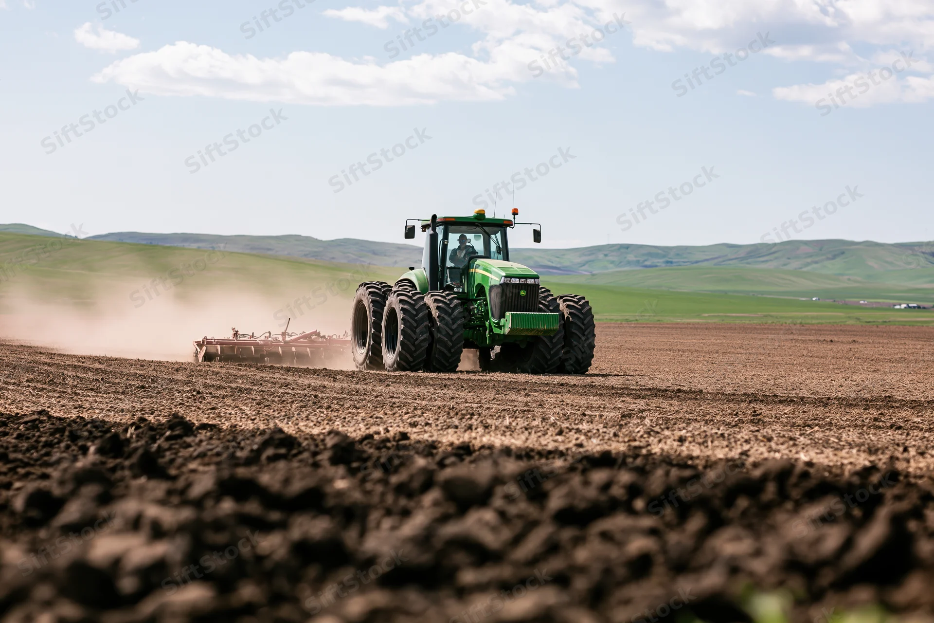 Green tractor pulling seeder across tilled field under partly cloudy sky