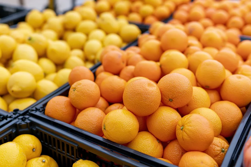 Lemons and mandarins piled high in black crates at an outdoor market fruit stall